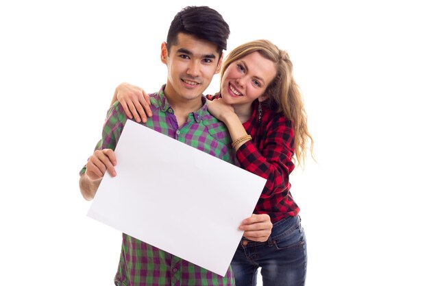 Young positive woman with young pleasant man with dark hair in plaid shirts holding white placard