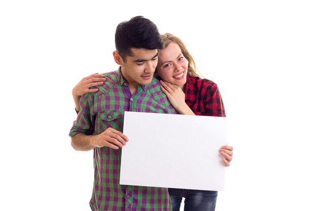 Photo young positive woman with young pleasant man with dark hair in plaid shirts holding white placard