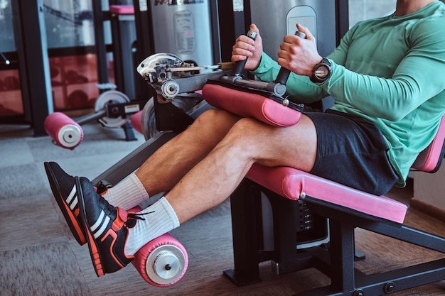 Young powerful man is doing legs exercises on training apparatus in gym