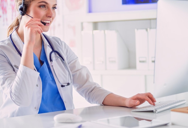 Young practitioner doctor working at the clinic reception desk she is answering phone calls and scheduling appointments