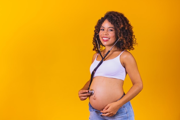 Una giovane donna afro incinta con lo stetoscopio che ascolta il bambino