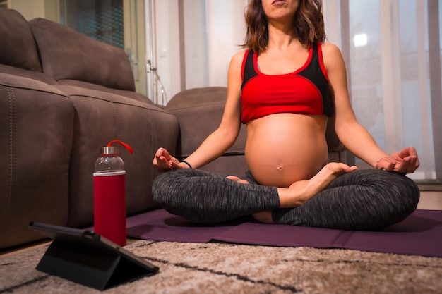 Young pregnant caucasian brunette doing yoga relaxation exercises at home Online exercises in prepartum classes wellness during pregnancy