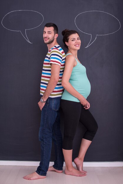 Young pregnant couple thinking about names for their unborn baby and writing them on a black chalkboard