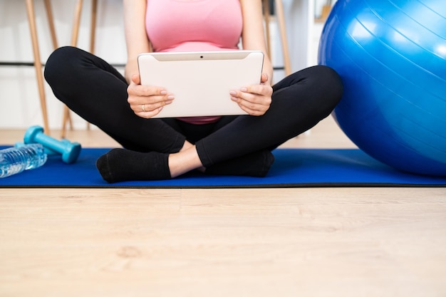 Young pregnant female using mobile device during working out in living room at home caucasian woman