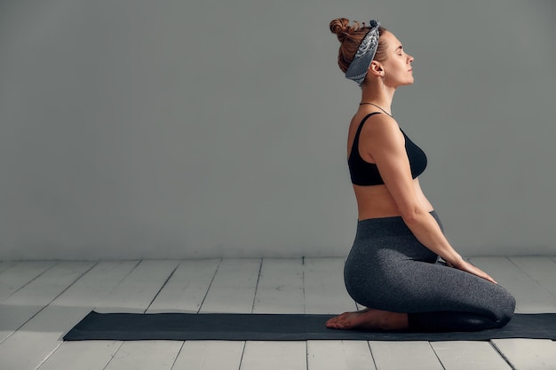 Young pregnant millennial woman sitting on the mat touches her belly after performing prenatal and meditation exercises at a yoga class Concept of life and maternity