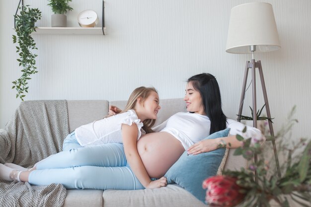 Young pregnant mother and her little daughter indoors