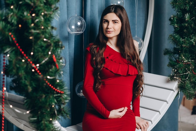 Молодая беременная мать сидит на качелях в рождественской атмосфере