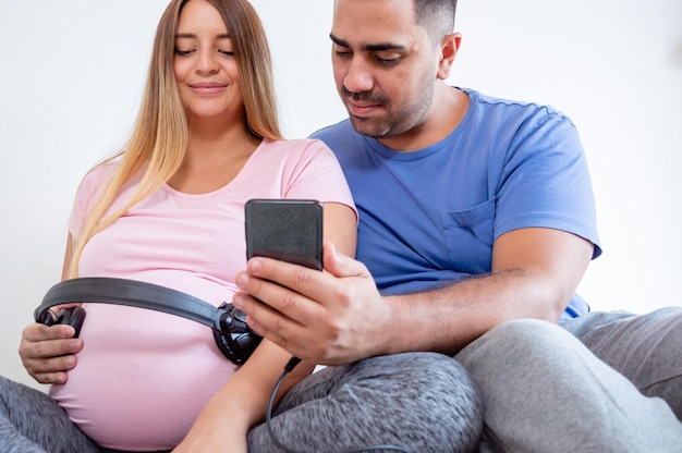 young pregnant venezuelan couple teaching music to their baby with headphones on his belly