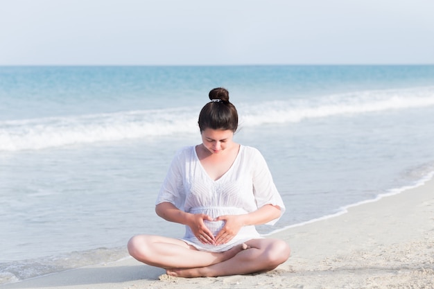 Young pregnant woman on the beach near blue sea and breathing