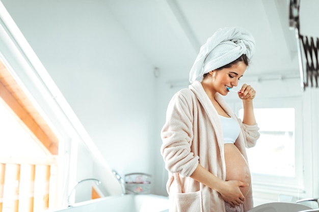 Young pregnant woman brushing her teeth in a bathroom