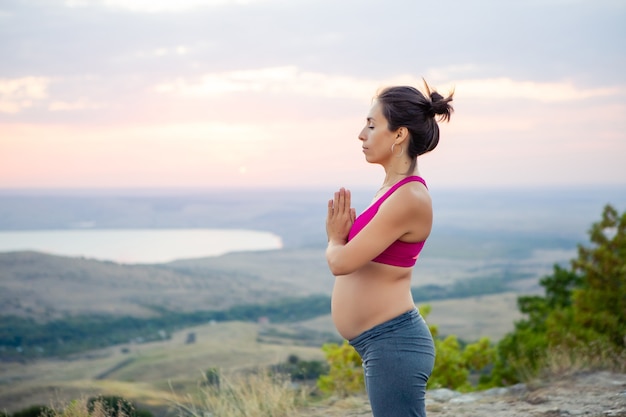 Young pregnant woman does yoga outdoors