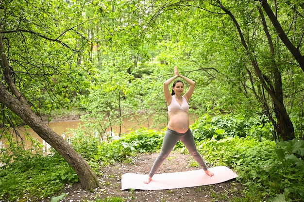 Foto giovane donna incinta che fa yoga che si esercita nel parco all'aperto