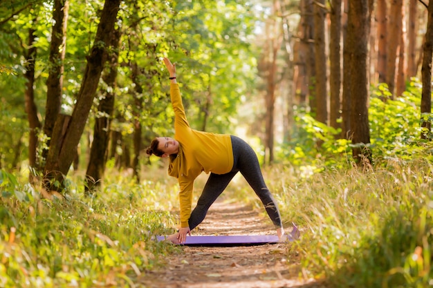 young pregnant woman doing yoga in the summer in the forest