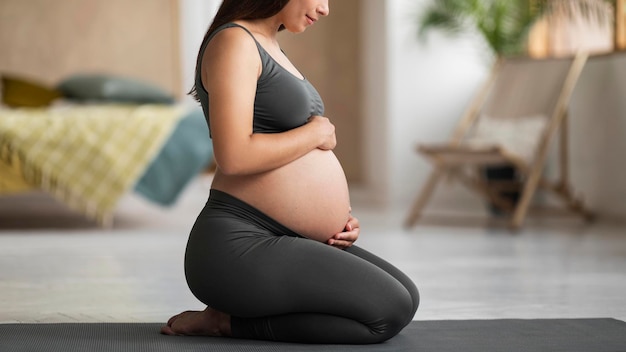 Young Pregnant Woman Embracing Belly While Sitting On Yoga Mat At Home