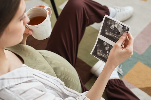 차 한 잔을 즐기고 소파에 앉아 아기의 초음파를 보는 젊은 임산부