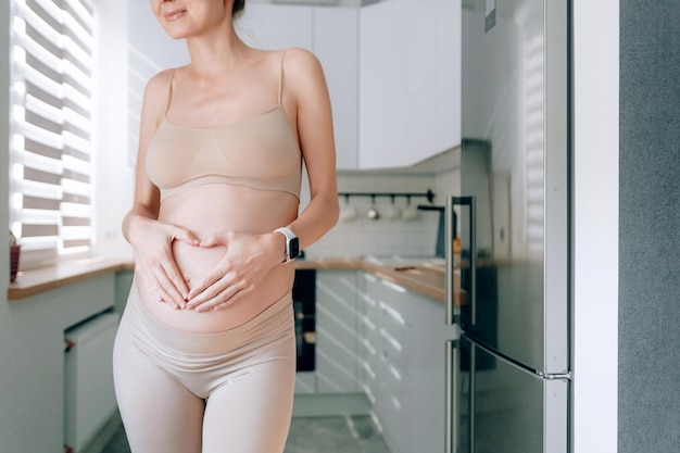 A young pregnant woman of European appearance in her kitchen with an avocado in her hands the concept of proper nutrition of pregnant women for the correct development of the fetus