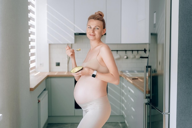 A young pregnant woman of European appearance in her kitchen with an avocado in her hands the concept of proper nutrition of pregnant women for the correct development of the fetus