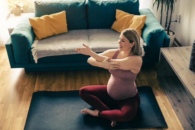 Photo young pregnant woman exercising yoga at home in the morning. she is doing stretching workout.