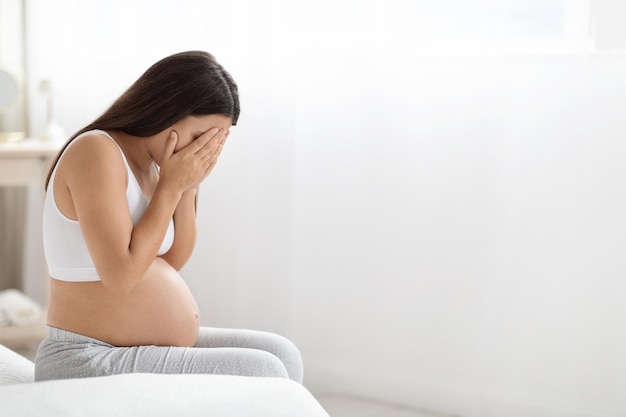 Young pregnant woman feeling sad crying at home