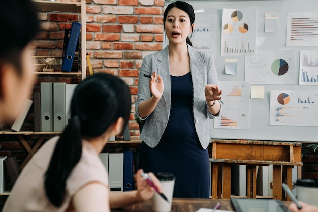 Young pregnant woman giving presentation to colleagues at
workplace. bokeh view of man and female coworkers sitting at table
in board room. future parent lady standing and talking in meeting
office