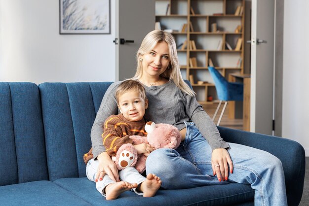 Young pregnant woman and her son sit on sofa at home little boy spend time together enjoy communication feeling kicks of unborn baby