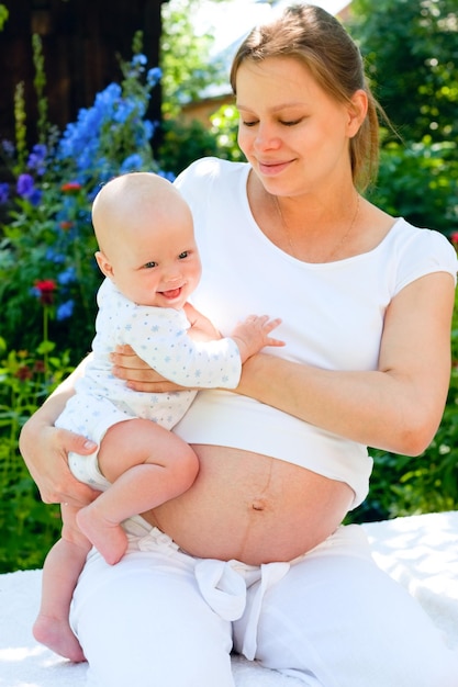Young pregnant woman holding baby girl in a summer garden