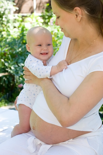 夏の庭で女の赤ちゃんを保持している若い妊婦