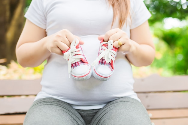 彼女の腹に赤ちゃんの靴を持っている若い妊婦