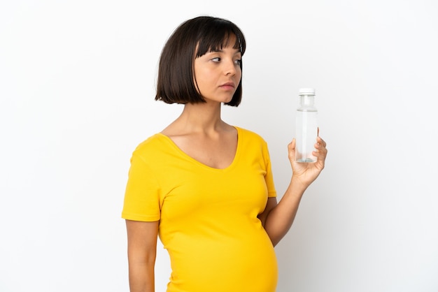 Young pregnant woman holding a bottle of water isolated on white background looking to the side