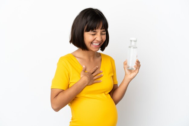 Giovane donna incinta che tiene una bottiglia di acqua isolata su fondo bianco che sorride molto