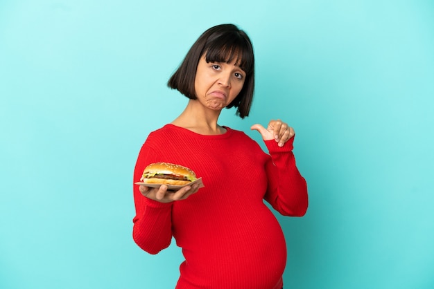誇りと自己満足の孤立した背景の上にハンバーガーを保持している若い妊婦