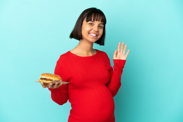 격리된 배경 위에 햄버거를 들고 행복한 표정으로 손으로 경례하는 젊은 임산부