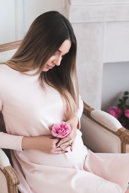 Young pregnant woman holding fresh pink rose flower