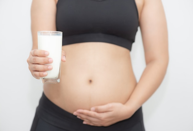 Foto giovane donna incinta che tiene un bicchiere di latte sulla mano destra e che tocca la sua pancia con cura sulla mano sinistra.