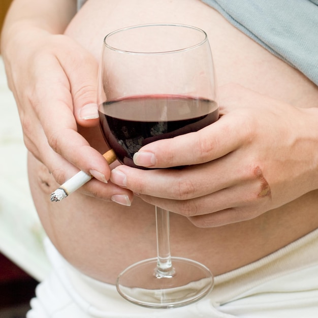 Young pregnant woman holding wine and cigarette