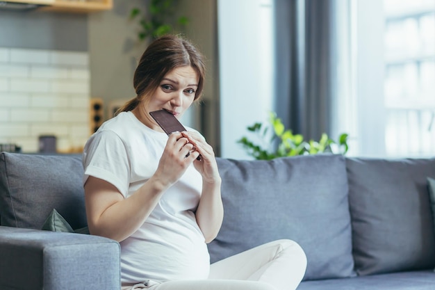 チョコレートを食べてソファに座って自宅で若い妊婦