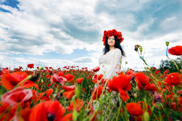 young pregnant woman is wearing wreath of flowers on poppy field