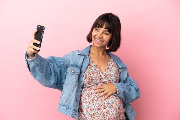 Young pregnant woman over isolated pink background making a selfie