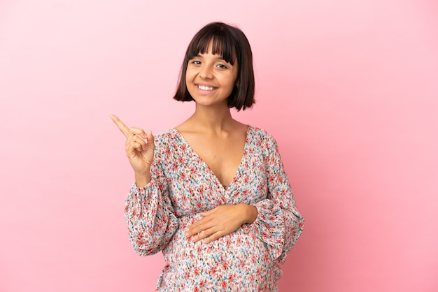 Young pregnant woman over isolated pink background pointing to the side to present a product