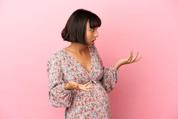 Young pregnant woman over isolated pink background with surprise expression while looking side