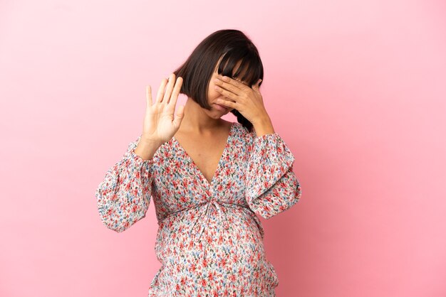 Young pregnant woman over isolated pink surface making stop gesture and covering face