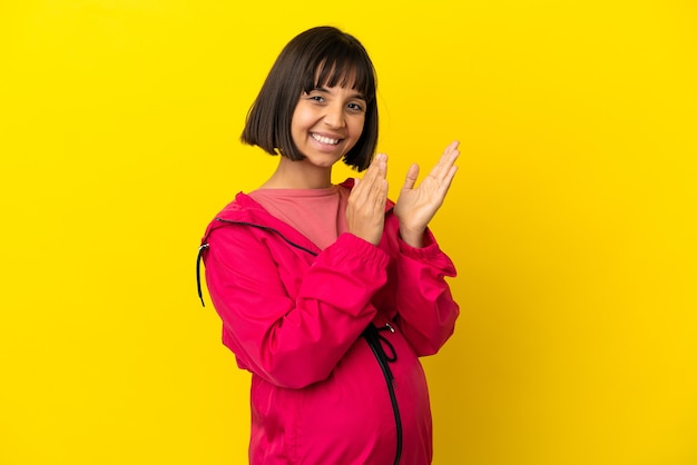 Young pregnant woman over isolated yellow background applauding after presentation in a conference