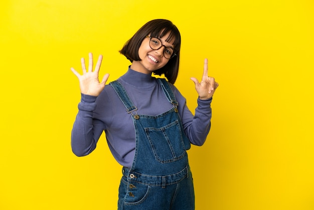 Young pregnant woman over isolated yellow background counting seven with fingers