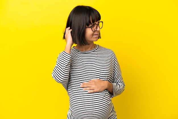 Young pregnant woman over isolated yellow background having doubts