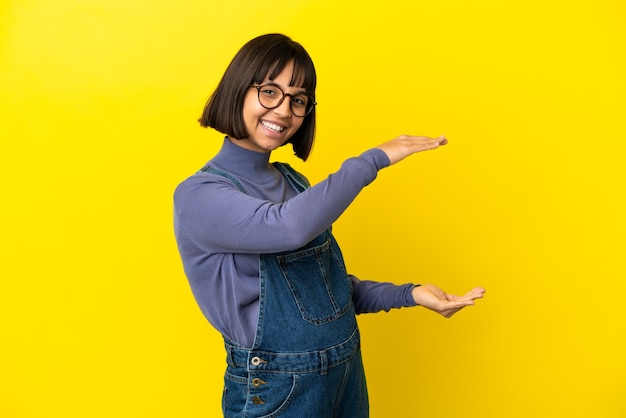 Young pregnant woman over isolated yellow background holding copyspace to insert an ad