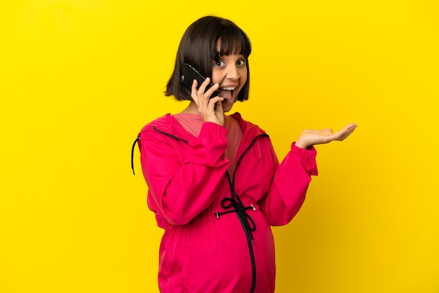 Young pregnant woman over isolated yellow background keeping a conversation with the mobile phone with someone