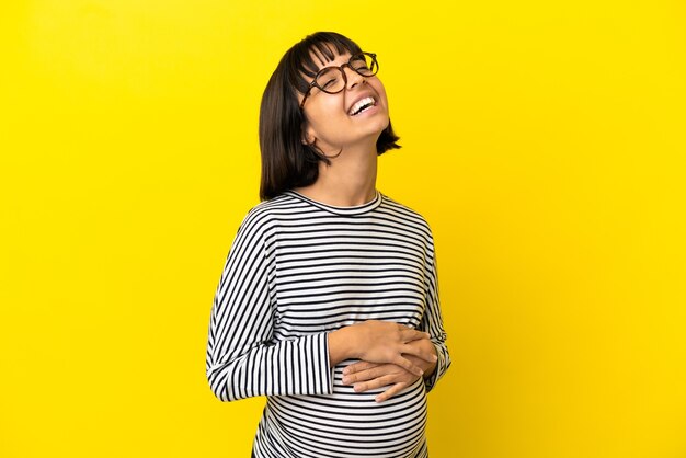 Молодая беременная женщина на изолированном желтом фоне смеется