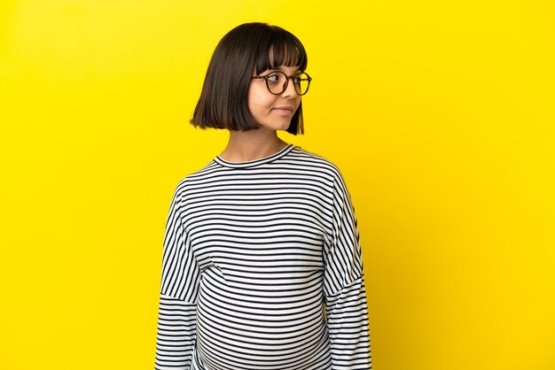 Young pregnant woman over isolated yellow background looking to the side