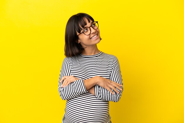 Young pregnant woman over isolated yellow background looking up while smiling