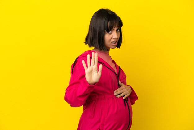 Young pregnant woman over isolated yellow background nervous stretching hands to the front